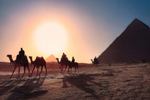 Camel riders crossing the sand in front of the Pyramids at sunset