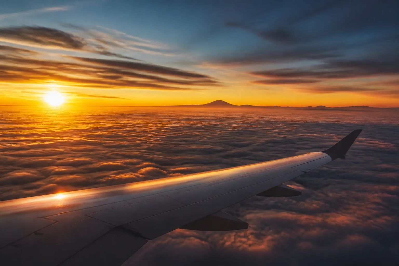 Aerial view of an aircraft wing above a soft layer of cloud at golden hour.