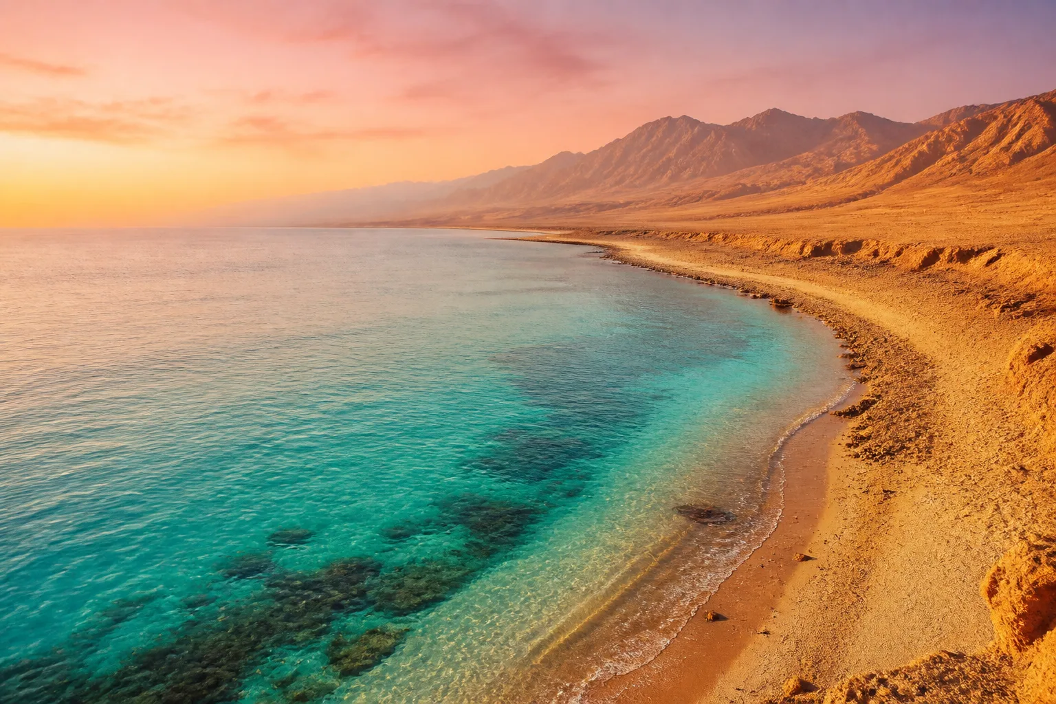 Calm turquoise sea meeting golden desert coast at sunrise, no buildings visible.